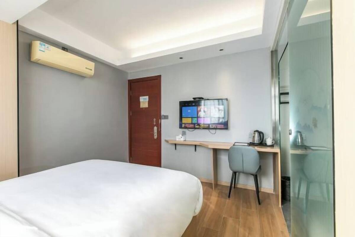 Habitació d'hotel amb llit, escriptori, cadira, televisió i una paret de vidre.