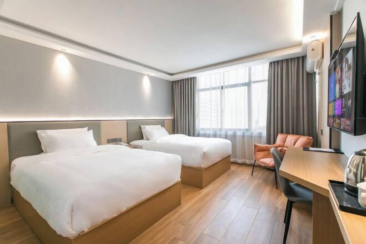Habitació d'hotel amb dos llits, un escriptori, una cadira, un televisor i una finestra amb cortines.