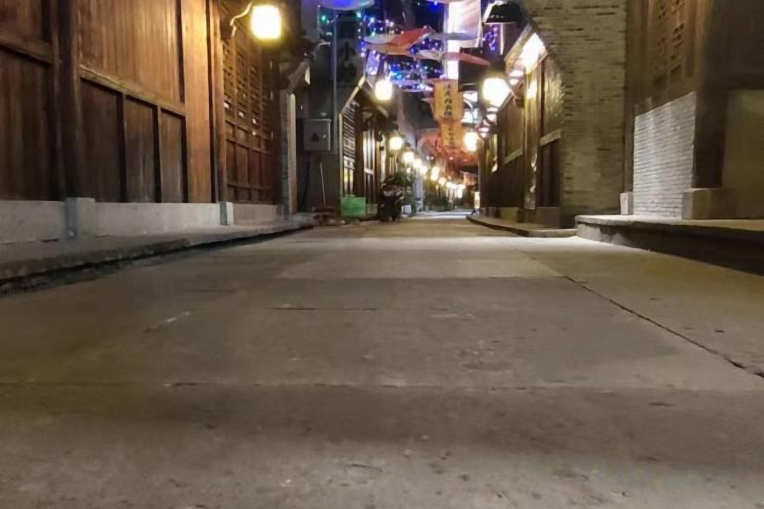 Una calle estrecha flanqueada por edificios, iluminada por luces colgantes.