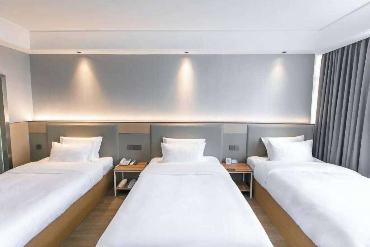 Habitació d'hotel amb tres llits individuals, cadascun amb una petita taula de nit de fusta i un telèfon.