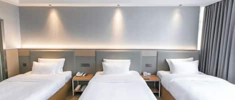 A hotel room with three single beds, each with a wooden nightstand and a telephone.