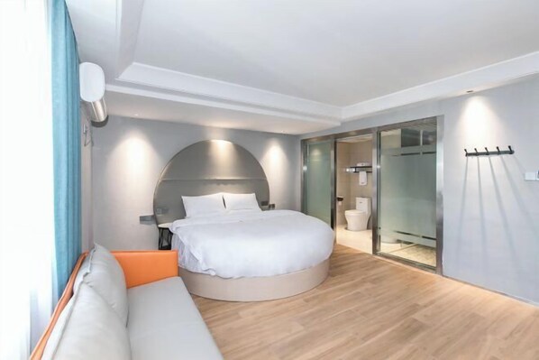 A modern bedroom with a round bed, a sofa, and a glass door leading to a bathroom. - 123 Hotel (Taizhou)