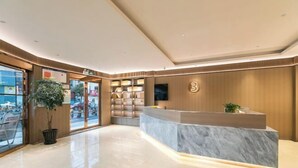 Eine moderne Hotelhalle mit einer Marmorrezeption, Holzvertäfelung und einer großen Küstpflanze.