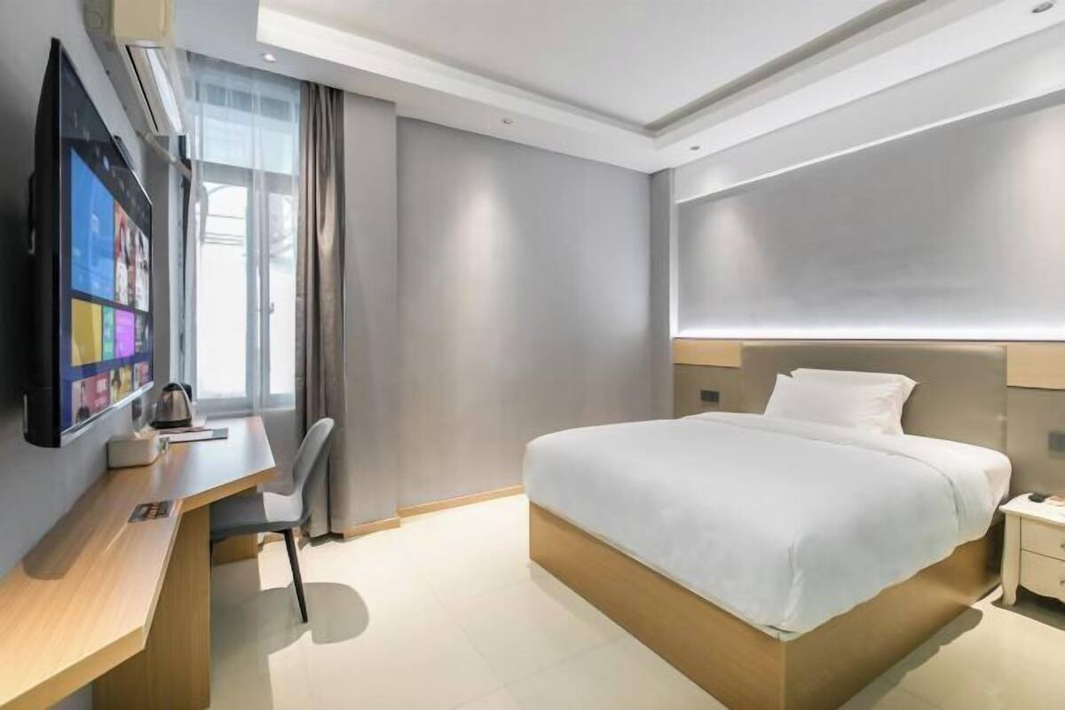 Habitació d'hotel moderna amb un llit gran, escriptori, televisió de pantalla plana i finestra amb cortines.