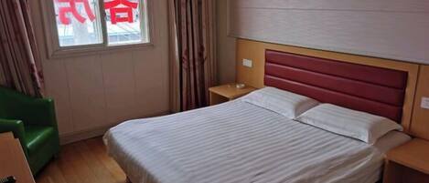A hotel room with a bed, a green chair, a nightstand, and a window with curtains.