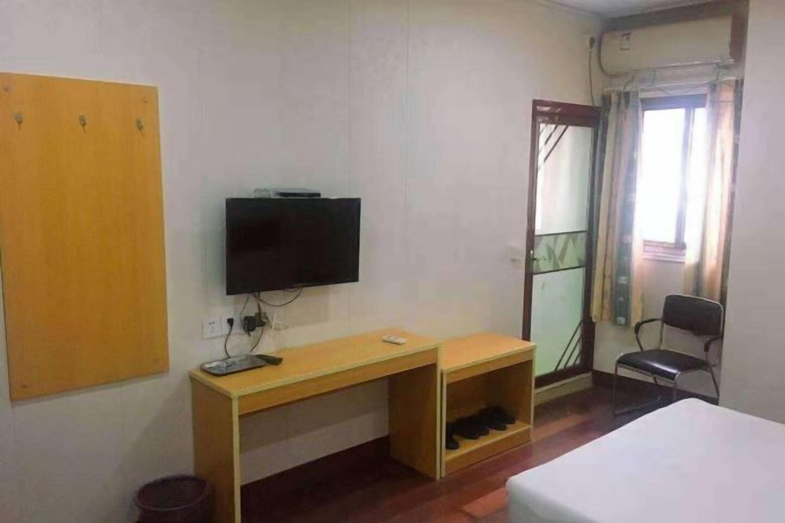 A room with a bed, a desk with a computer, a TV, a chair, and a door.