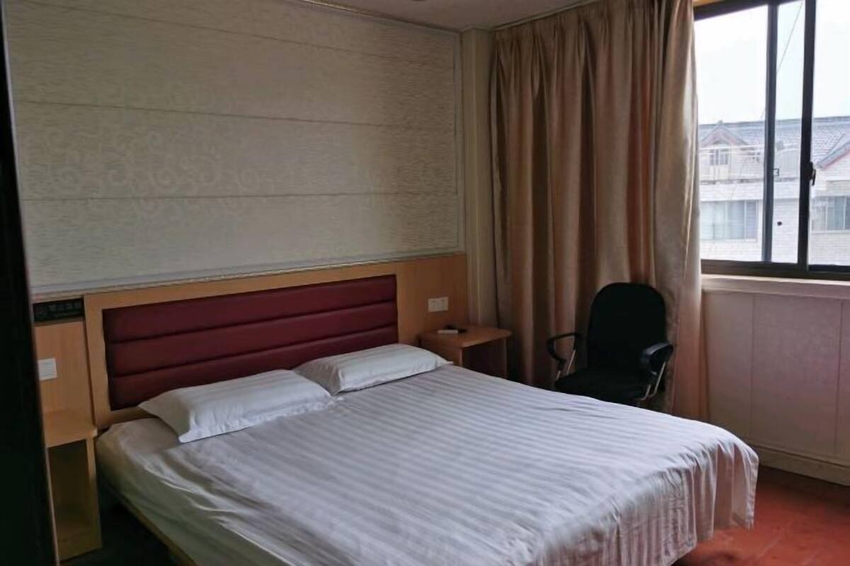 A hotel room with a bed, a chair, a nightstand, and a window with curtains.