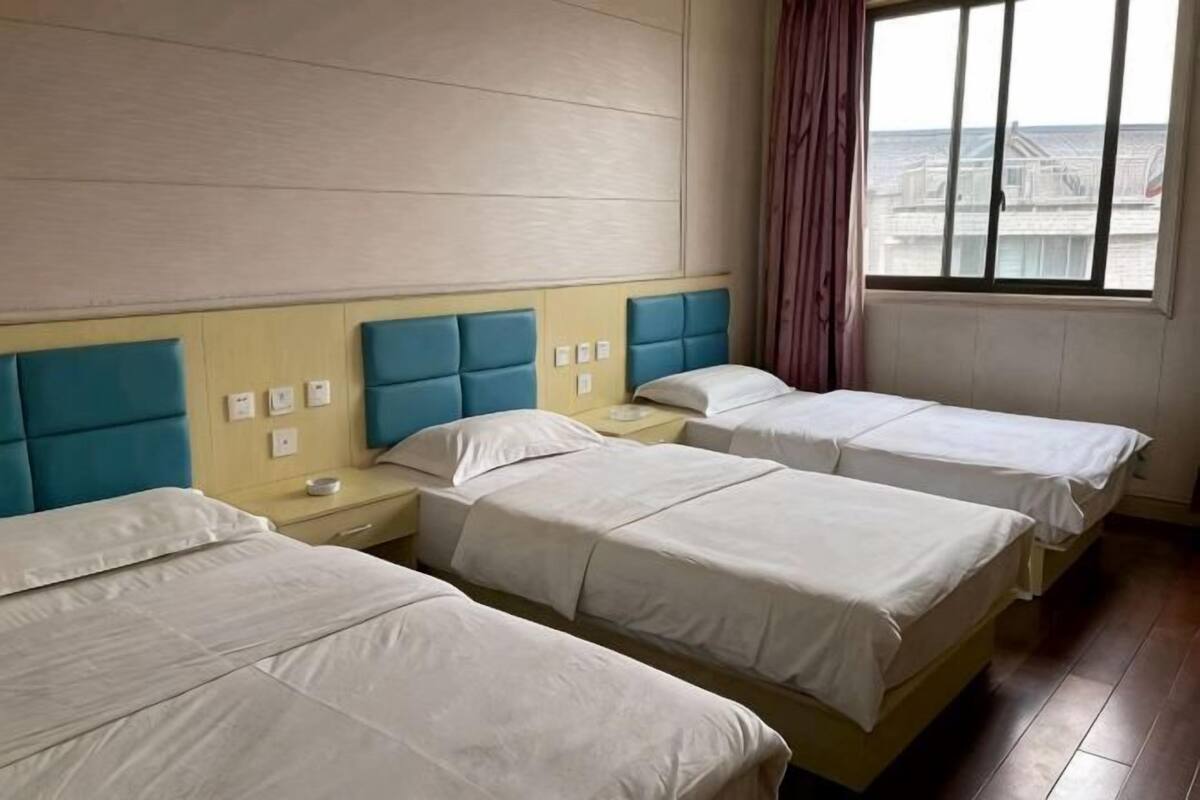 A hotel room with three beds, a wooden headboard, a window with a view, and a curtain.