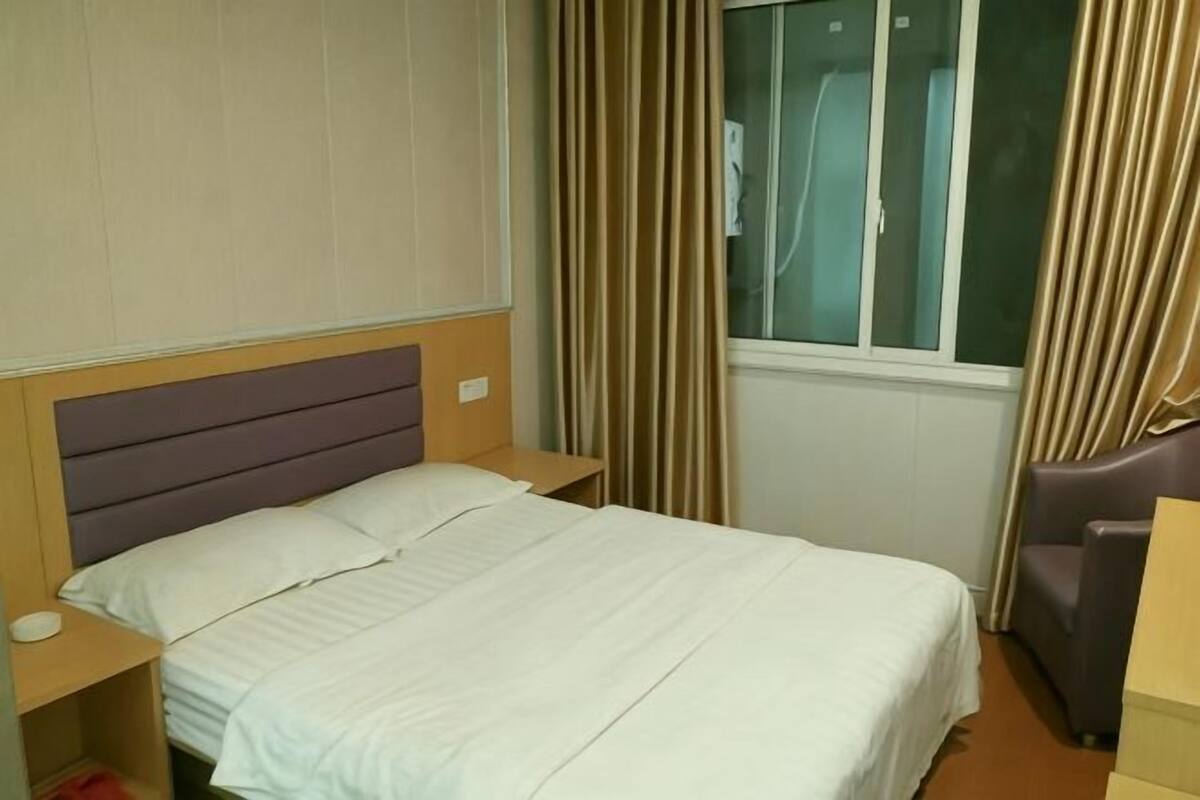 A hotel room with a bed, nightstand, chair, and window with curtains.
