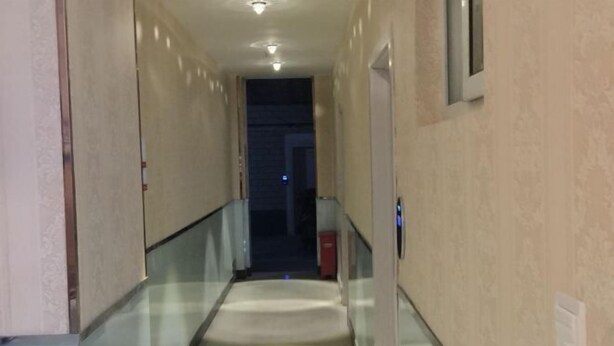 A corridor with a glass railing, beige walls, and a door at the end.
