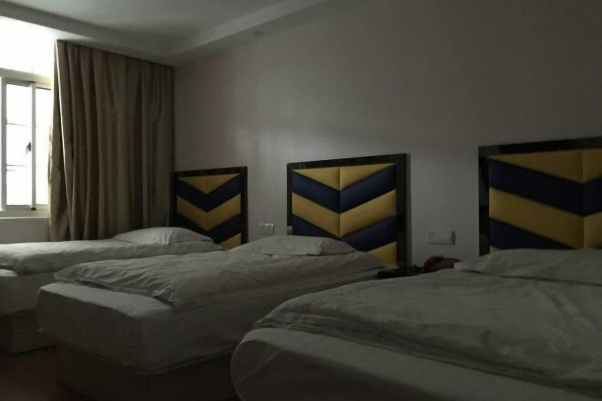 A hotel room with three beds, a window with curtains, and a wall with a geometric headboard design.