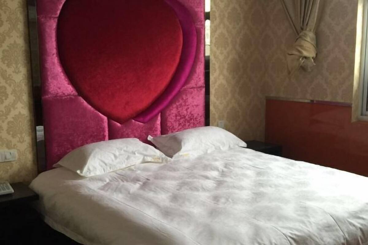 A bed with a red headboard, white bedding, and a patterned wall.