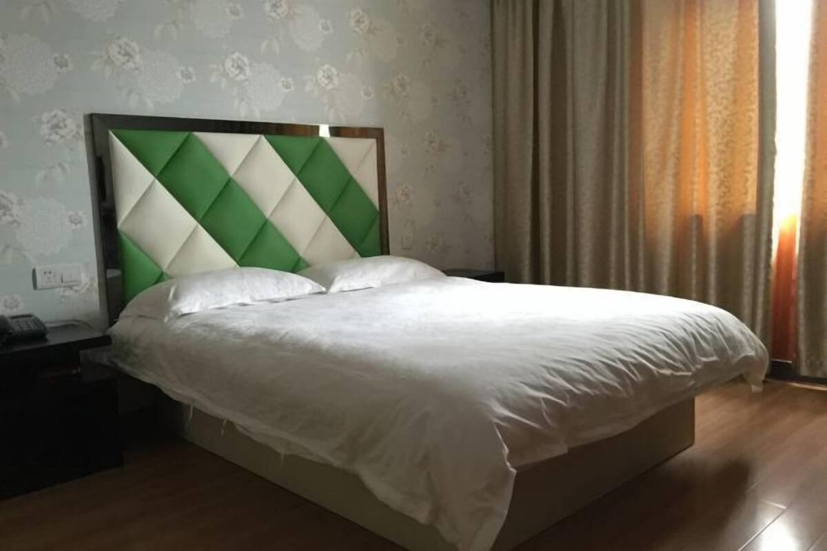 A neatly made bed with a green and white headboard, a bedside table with a phone, and a window with curtains.