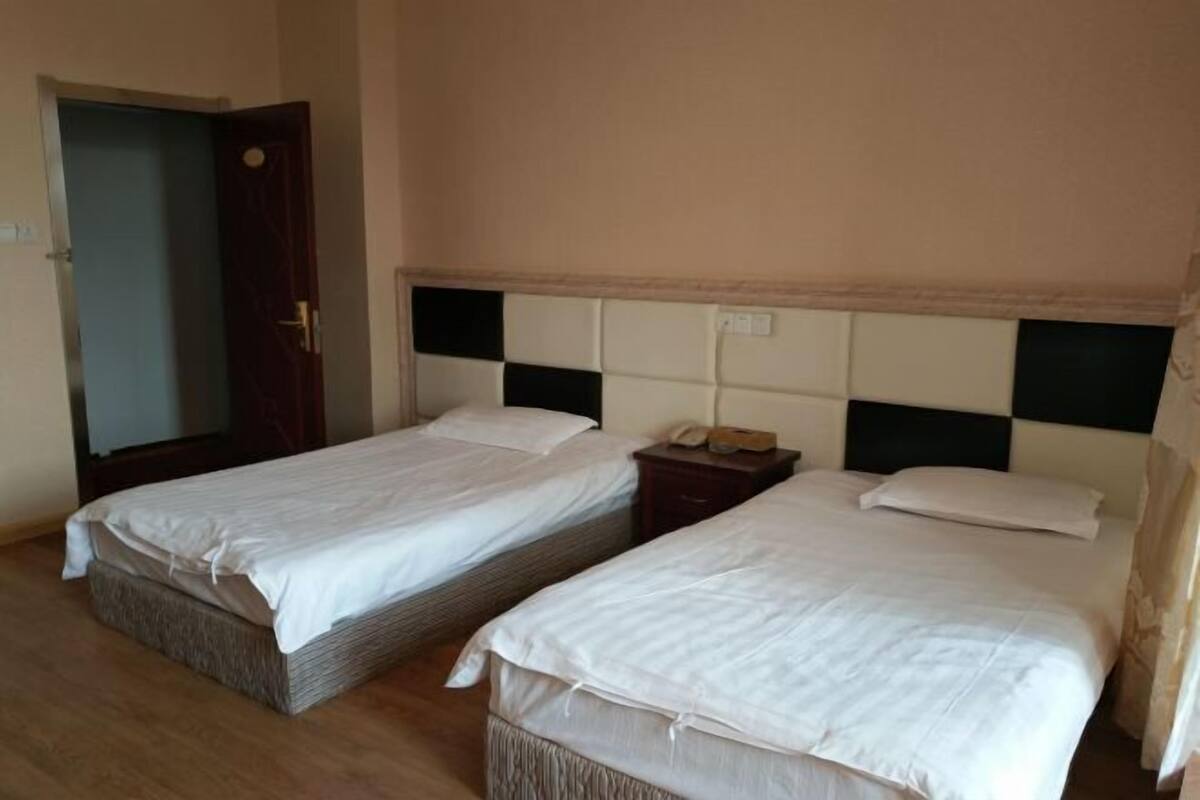 A room with two single beds, a wooden floor, a door, and a nightstand with a phone.