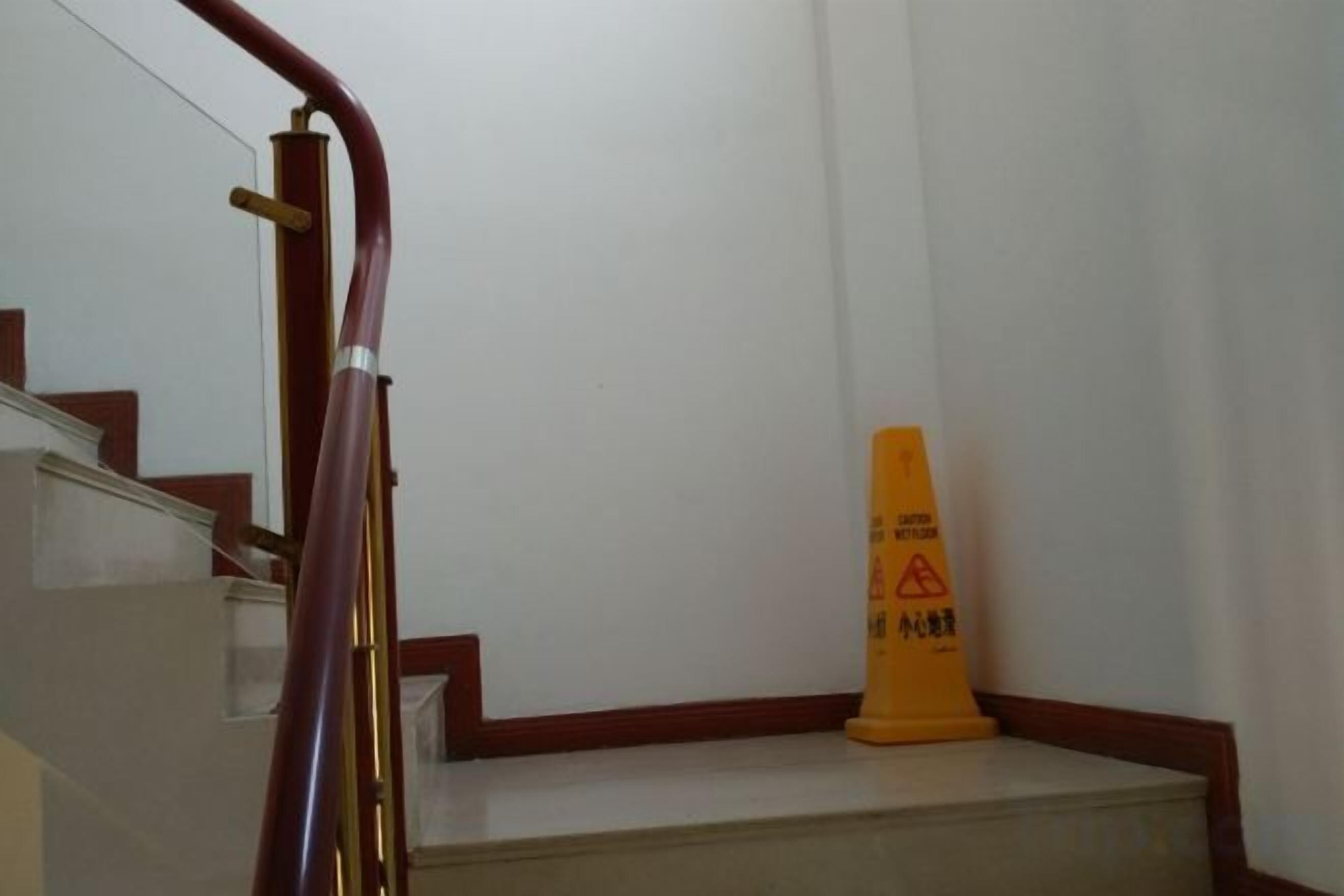 Una escalera con barandilla y un cono amarillo de precaución al final.