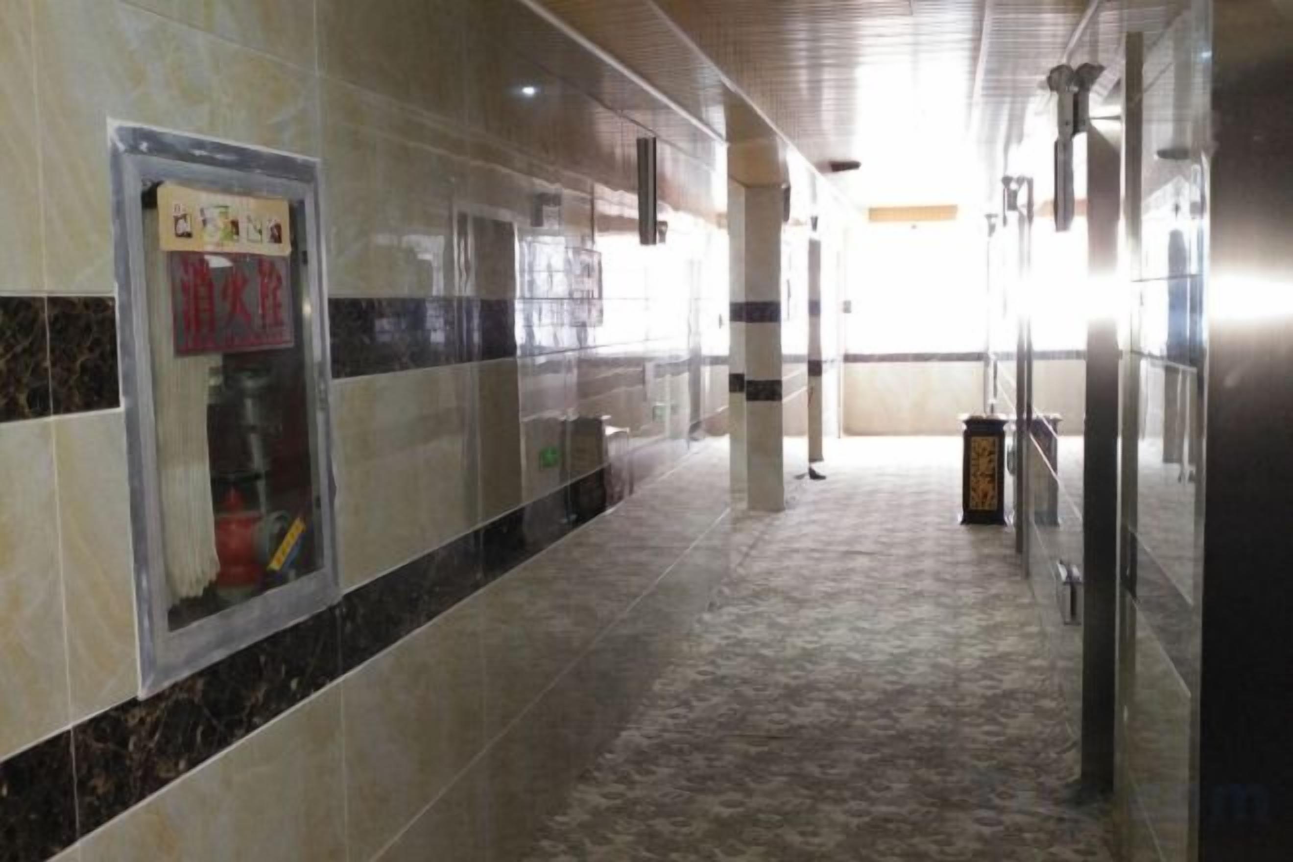 A corridor with tiled walls, a fire extinguisher, and a trash bin.
