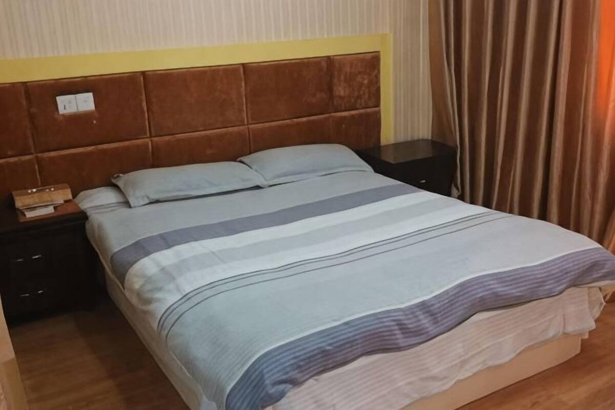 A bed with a striped bedspread, a wooden headboard, a nightstand with a lamp, and a curtain.