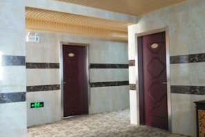 A hallway with two doors, one with a green exit sign, and a textured ceiling. - DONG FANG LUO MA (Wuhu)