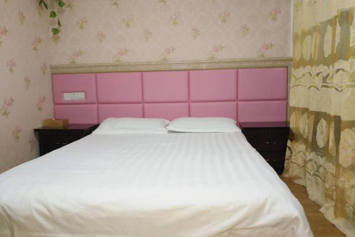 A bed with a pink headboard, white bedding, and a floral-patterned wall.