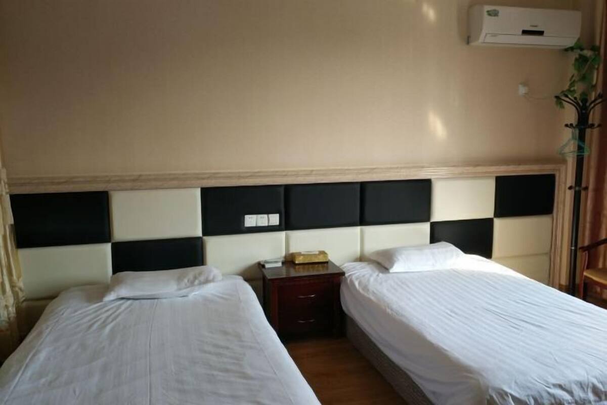A hotel room with two beds, a nightstand, and an air conditioning unit on the wall.