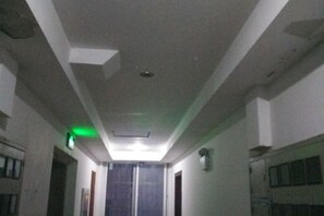 A narrow hallway with a ceiling that has a recessed light fixture and a green emergency exit sign. - DONG FANG LUO MA (Wuhu)