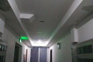 Um corredor estreito com luminária embutida no teto e placa de saída de emergência verde.