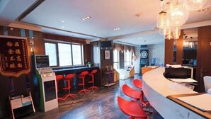 A modern hotel lobby with a reception desk, red bar stools, and a large window providing natural light.
