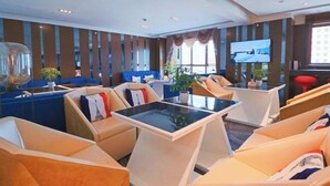 A modern hotel lobby with seating areas, a flat-screen TV, and large windows.