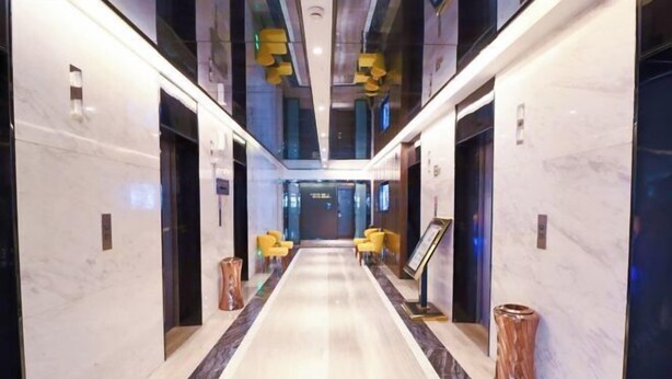 A modern hotel lobby with marble floors, yellow chairs, and a central reception desk.