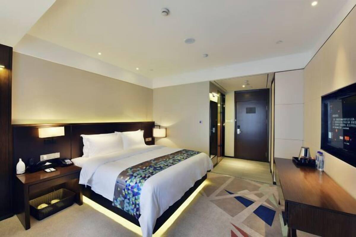 A hotel room with a bed, bedside table, lamp, and a television.