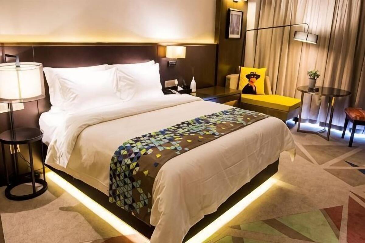 A hotel room with a bed, bedside tables, a lamp, a chair, and a small table with a plant.