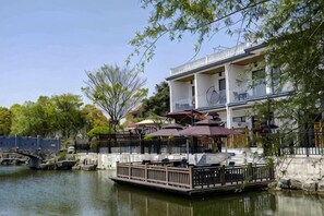 Um restaurante à beira-rio com mesas ao ar livre, uma ponte ao fundo e um edifício com varandas.