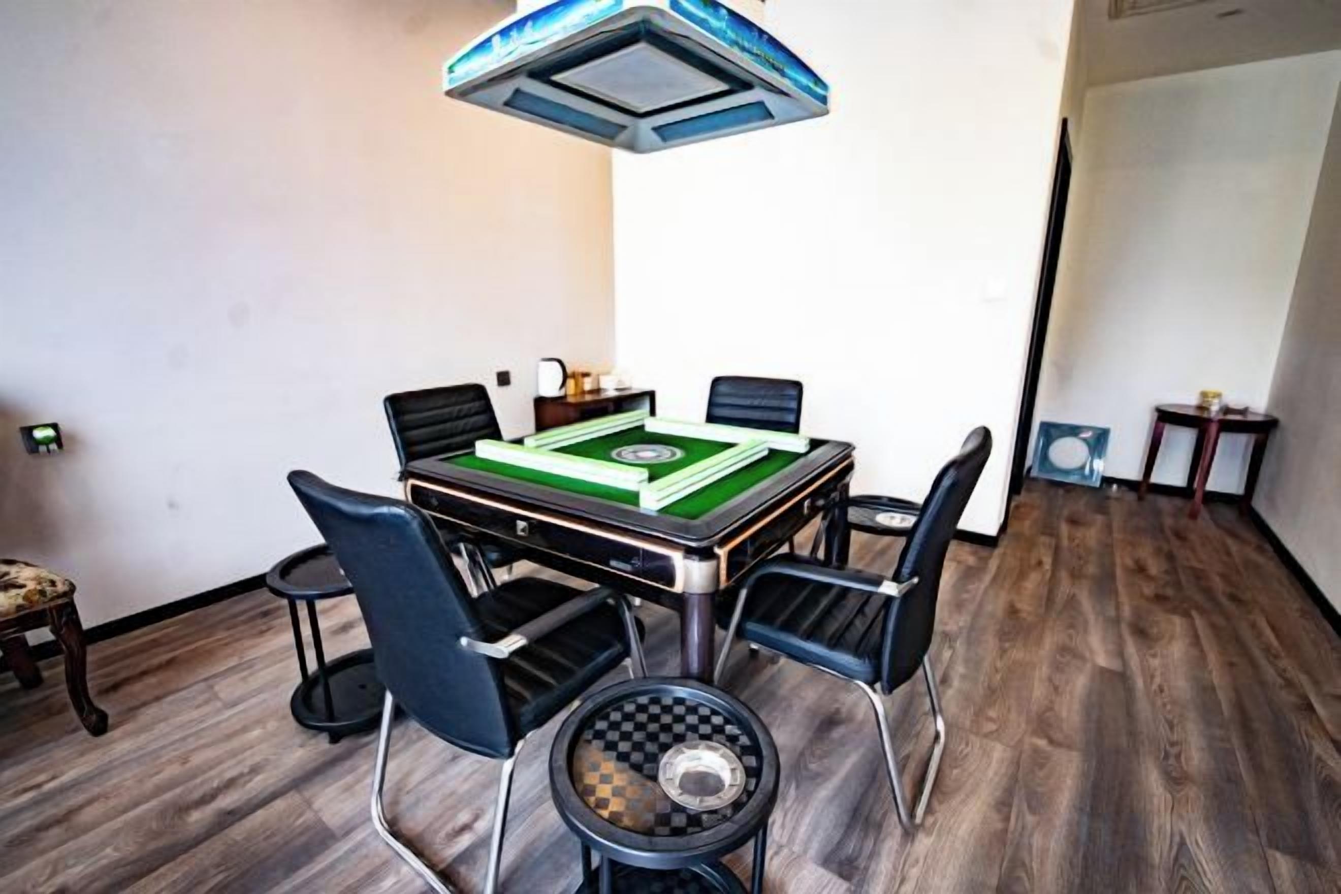 A room with a table set for a game, four chairs, a small side table, and a ceiling light fixture.