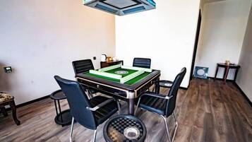 A room with a table set for a game, four chairs, a small side table, and a ceiling light fixture.