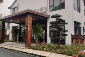 A building with a covered entrance, potted plants, and a well-maintained garden. - Donglai Manor Hotel (Shanghai)