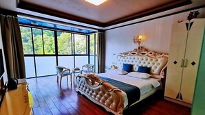 Ein Schlafzimmer mit einem großen Bett, einem Sessel, einem Kleiderschrank und Blick auf Grünpflanzen durch ein Fenster.
