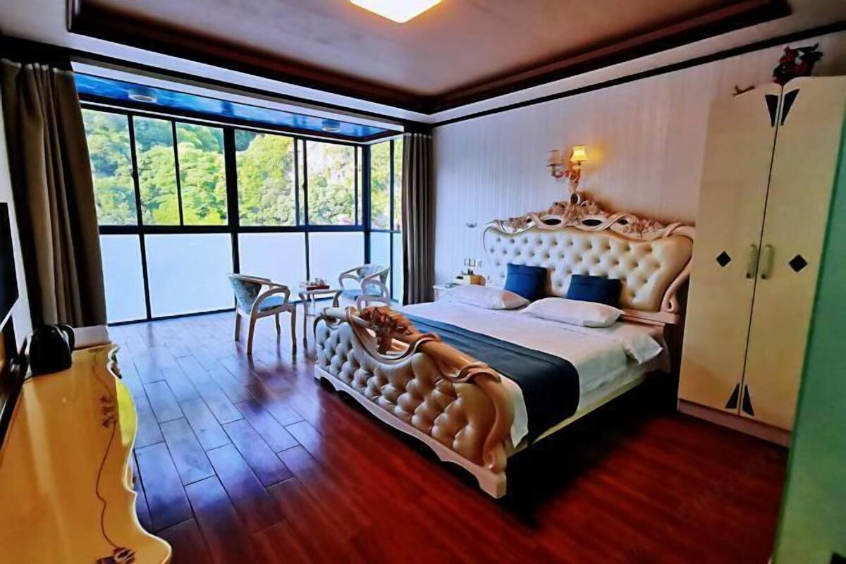Un dormitorio con una cama grande, una silla, un armario y vistas a zonas verdes a través de una ventana.