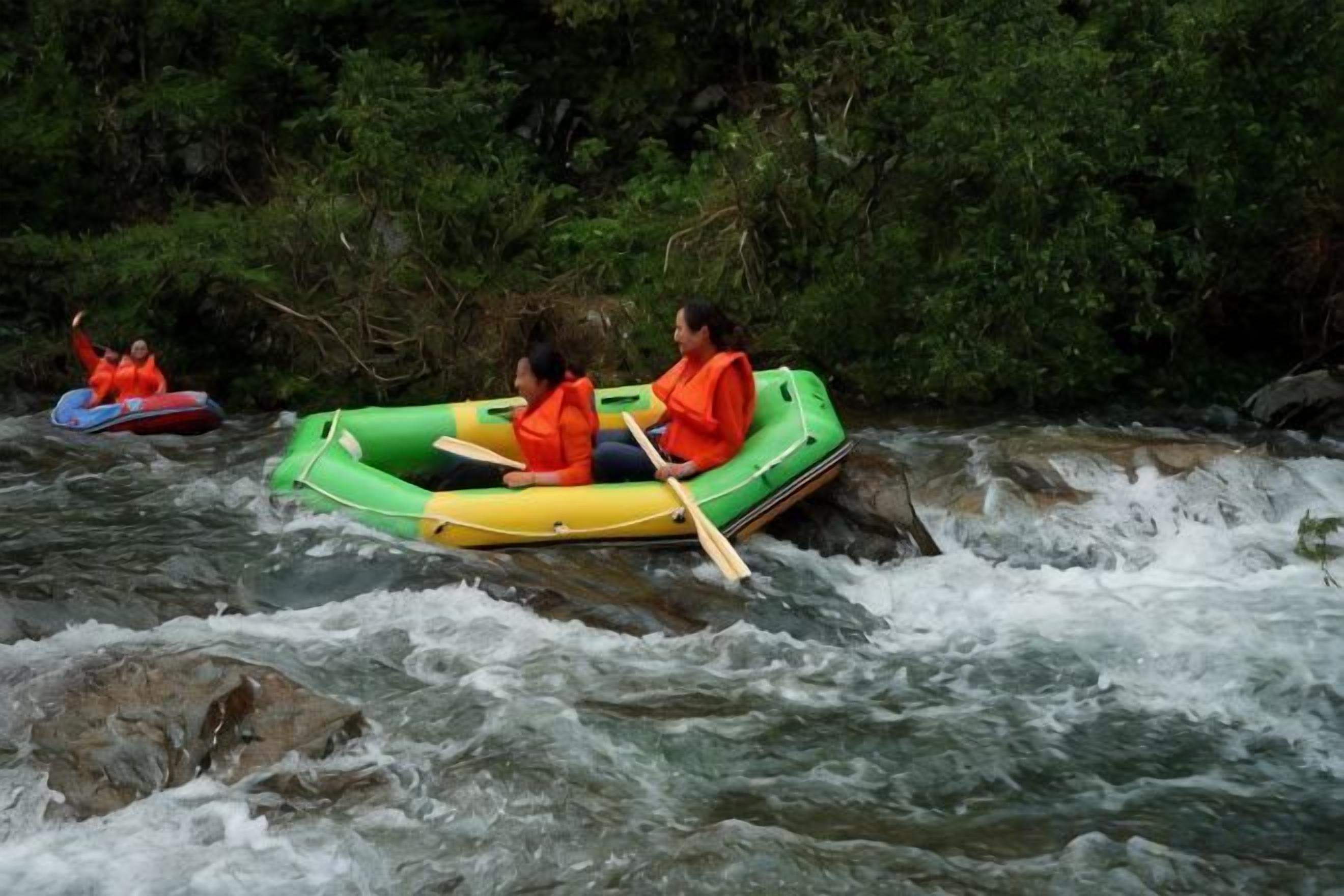 Two people in a green inflatable raft on a river with rapids.