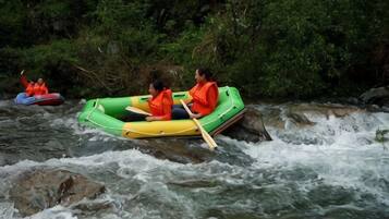 Two people in a green inflatable raft on a river with rapids.