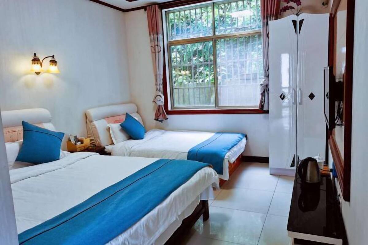 Una habitación con dos camas, un armario, un escritorio y una ventana con vistas al verdor.