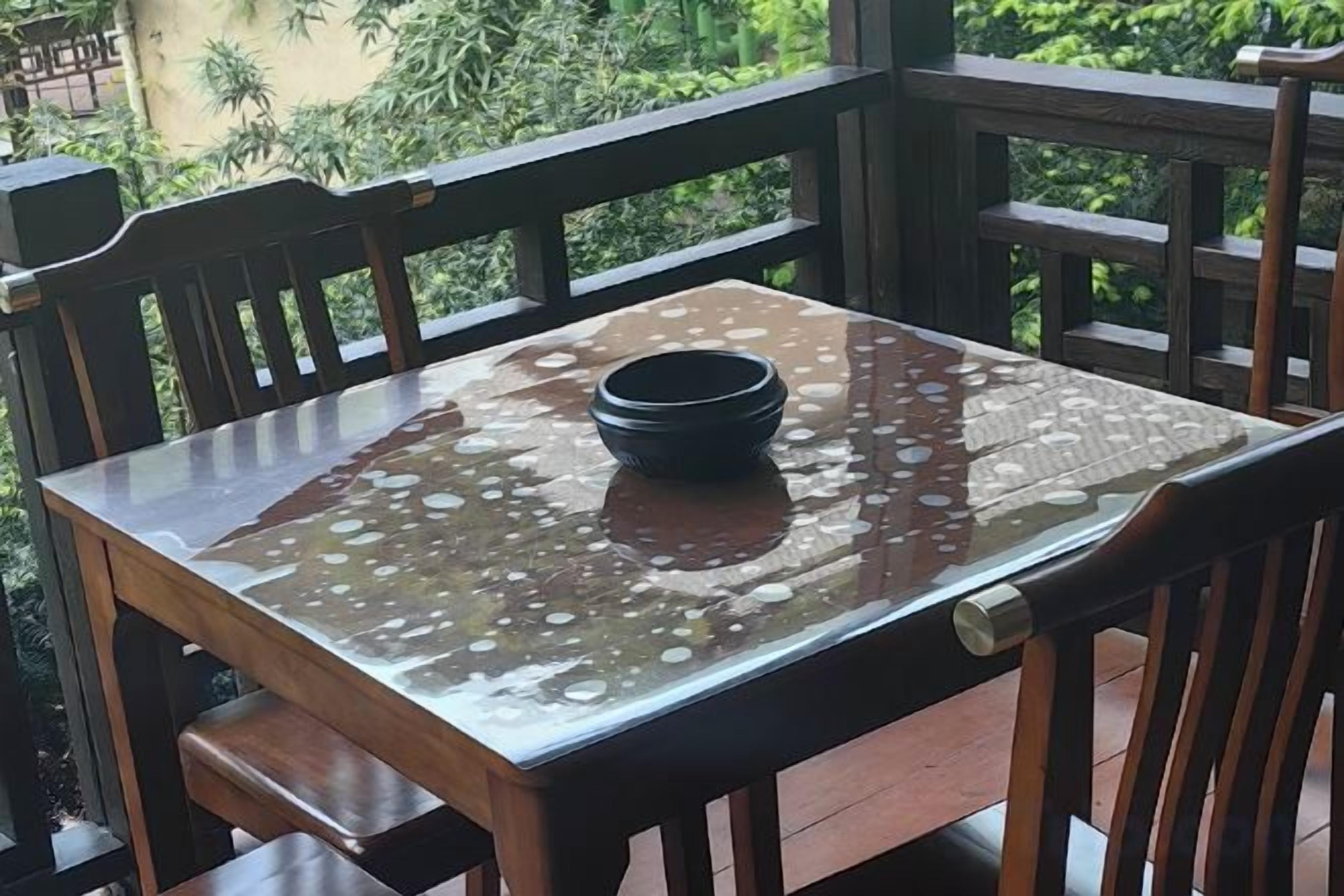 A wooden table with a glass top and a black bowl on it, set on a balcony with wooden railings.