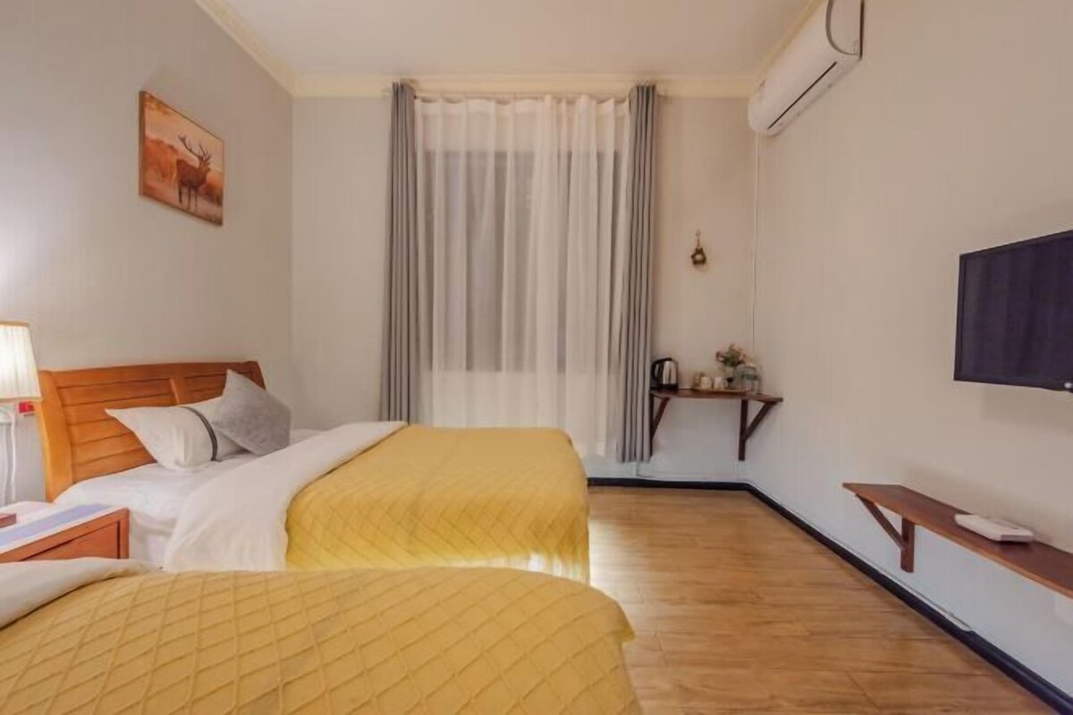 A hotel room with two beds, a TV, a desk, and a window with curtains.