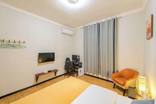 A hotel room with a bed, a desk with a computer, a chair, a TV, and a window with curtains. - Qingqing Inn (Dali City)