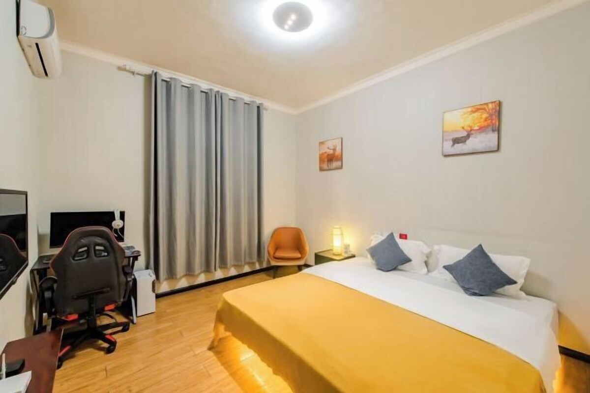 A hotel room with a bed, a desk with a computer, a chair, a desk lamp, and a window with curtains.