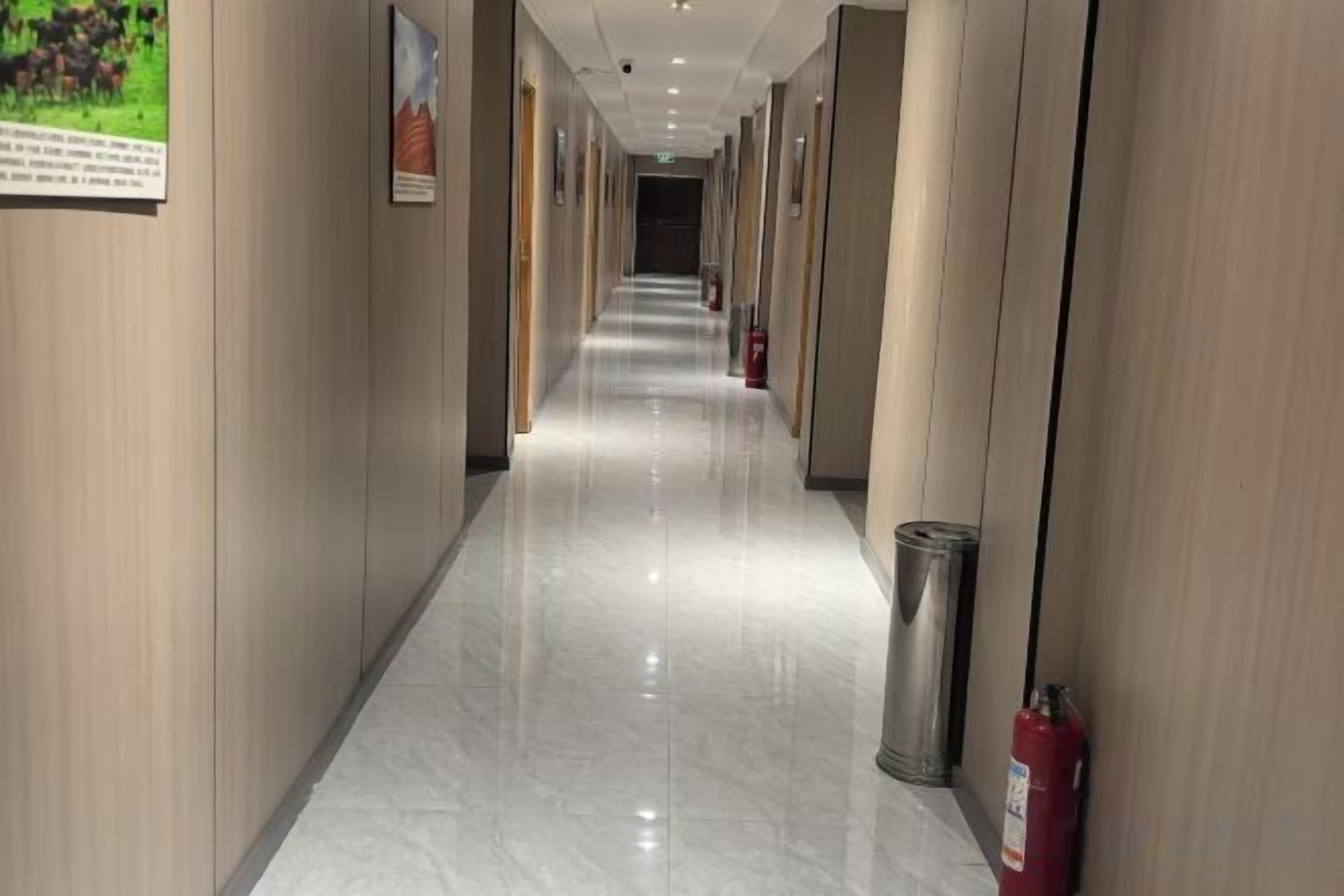 A hotel corridor with a polished floor, wooden paneling, and a fire extinguisher on the right.