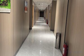 Pasillo de hotel con suelo pulido, paneles de madera y un extintor a la derecha.