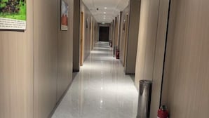 En lång, smal hotellkorridor med ett polerat marmorgolv, träpanel på väggarna och en brandsläckare på höger sida.