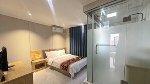 Ett hotellrum med en säng, ett nattduksbord, en TV och en duschavdelning med glasväggar.
