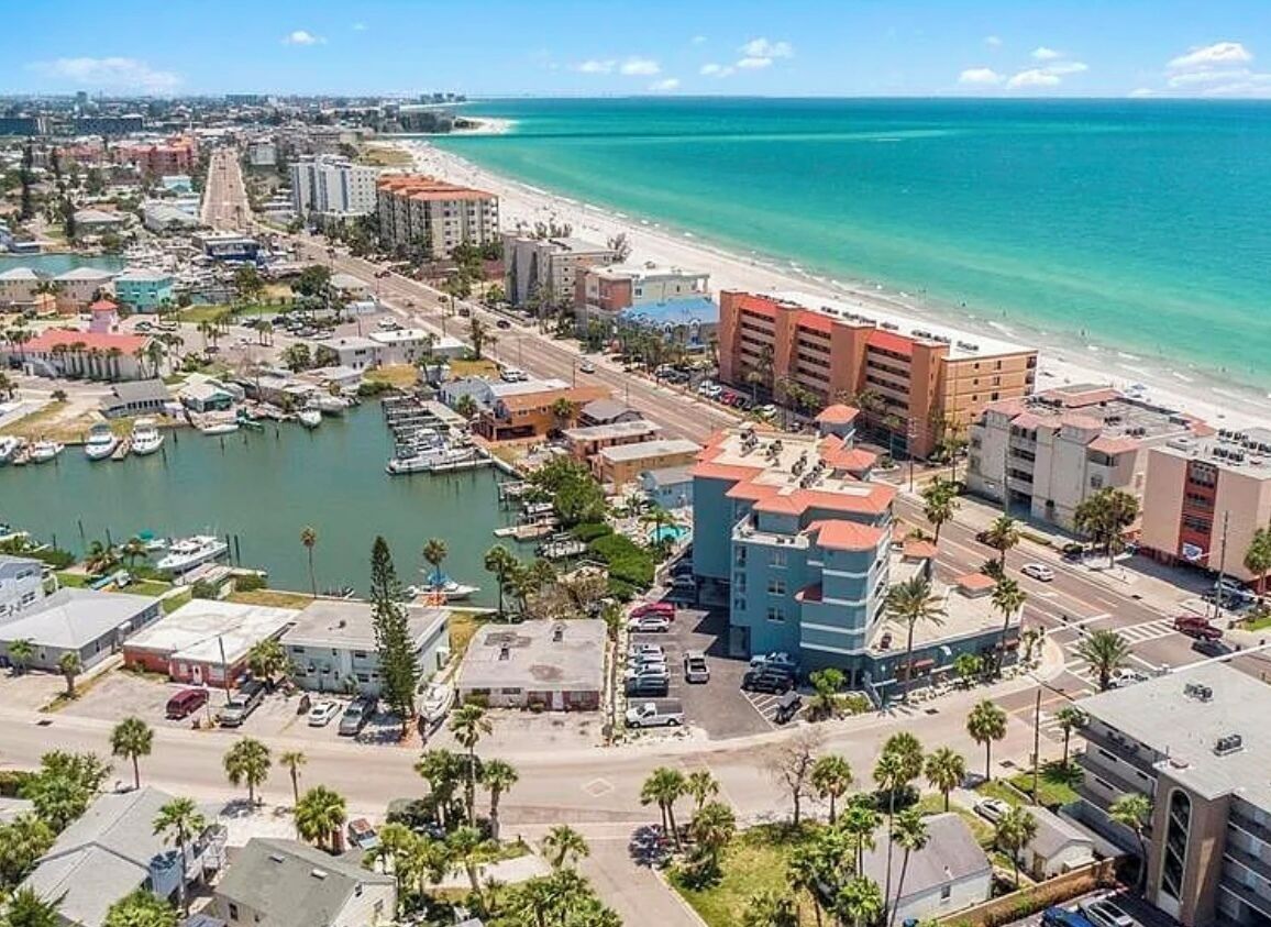 An aerial view of a coastal city with a marina, buildings, and a beach.