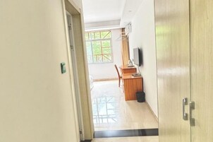 Un pasillo que conduce a un comedor con una mesa y sillas, un televisor montado en la pared y una puerta con picaporte.